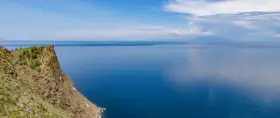 Majestatyczne jezioro w Rosji, z klifem porośniętym trawą i drzewami, w oddali widać góry.