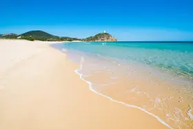 Piękne plaże Cagliari z turkusową wodą i piaszczystym brzegiem. W oddali widać wzgórze z wieżą.
