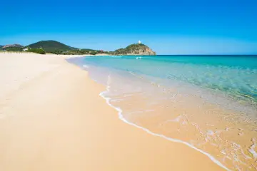 Piękne plaże Cagliari z turkusową wodą i piaszczystym brzegiem. W oddali widać wzgórze z wieżą.